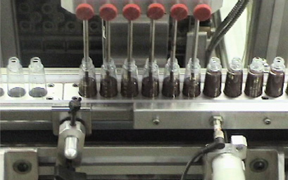 Machine filling cosmetic bottles and tubes from the bottom up.